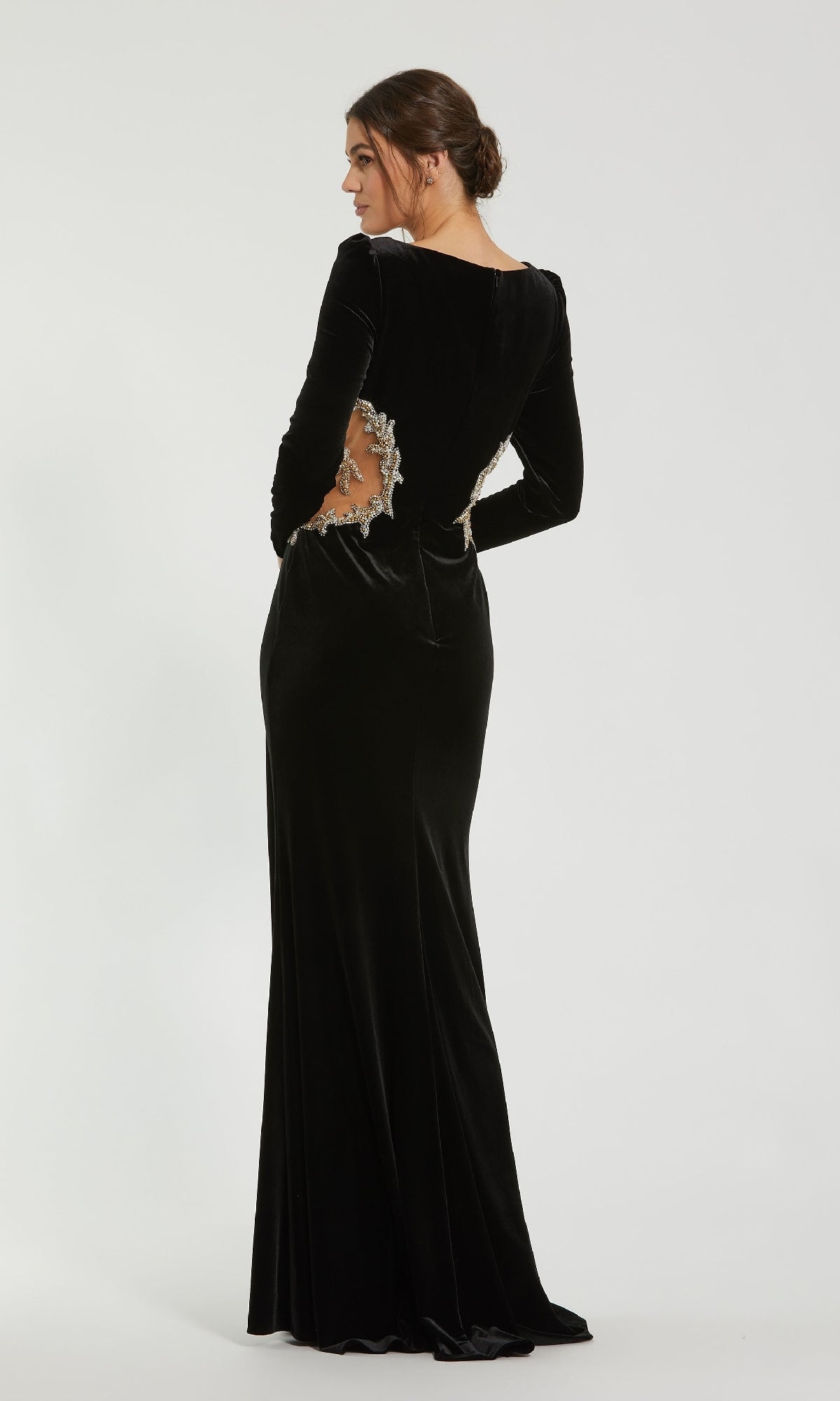A woman in the Mac Duggal 79445 long formal dress with beaded sheer midriff cutouts stands facing away, looking over her shoulder against a plain background.